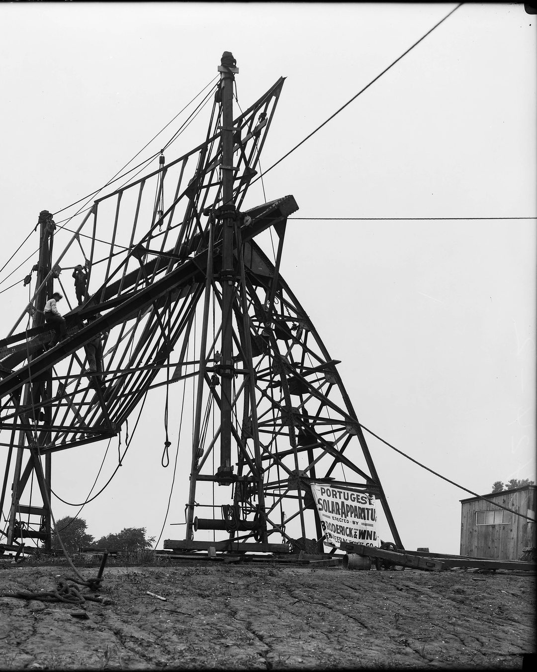 A máquina ainda reduzida à armação, com operários na estrutura e o cartaz «Portuguese Solar Apparatus». St. Louis, 5 de julho de 1904. Fotografia da Exposição Universal (St. Louis Public Library). Sem direitos de autor nos Estados Unidos.